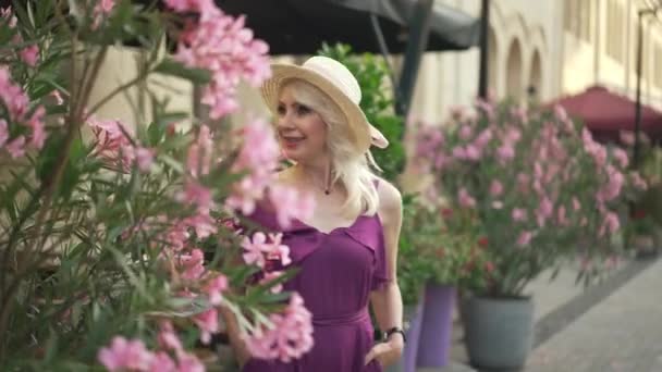 Elegante zelfverzekerde dame loopt naar de stad straat langs bloempotten en kijkt naar de camera glimlachend. Portret van vrolijke slanke mooie blanke vrouw wandelen in de ochtend in de Europese stad poseren. — Stockvideo