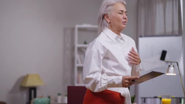 Зрелая женщина-бизнес-аналитик с болью в груди стоит в кабинете. Портрет нездоровой белой женщины средних лет в помещении. Здравоохранение и медицина. — стоковое видео