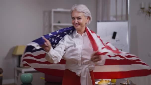 Trots zelfverzekerde vrolijke volwassen vrouw wikkelen in USA vlag kijken naar camera glimlachen. Portret van slanke prachtige blanke zakenvrouw poseren in het kantoor binnen in slow motion. — Stockvideo