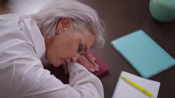 Vista de ángulo alto agotado mujer de negocios madura durmiendo en la mesa en la oficina. Hermosa mujer delgada de mediana edad caucásica cansada que duerme en el lugar de trabajo en el descanso. Cansancio y agotamiento. — Vídeos de Stock