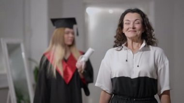 Heyecanlı bir beyaz anne evde poz veriyor ve geriye dönüp sertifikasını sarmış zeki bir doktora kızına bakıyor. Gülümseyen kameraya bakan mutlu mutlu bir kadının portresi. Destek ve istihbarat.