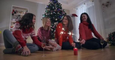 Yeni yılda dört mutlu kadının Noel ağacında parlak maytaplar ve gülümseyen şampanya bardaklarıyla oturması. Neşeli Kafkasyalı arkadaşlar tatillerini içeride kutluyorlar. Sinema 4k ProRes Merkezi.