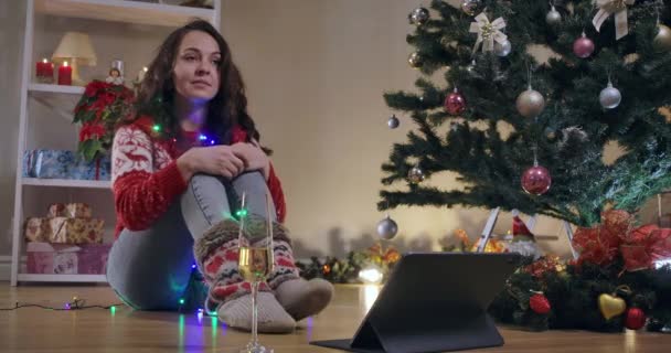Slim wanita muda yang gembira duduk di pohon Tahun Baru dengan lampu Natal menunggu keajaiban. Potret wanita milenial Kaukasia cantik yang berambut coklat menikmati liburan. Sinema 4k ProRes HQ. — Stok Video