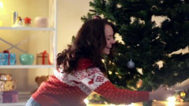 Yeni yıl ağacını evdeki oturma odasında süsleyen çekici beyaz kadın portresi. Mutlu gülümseyen güzel milenyum bayanı Noel için içeride hazırlanıyor..