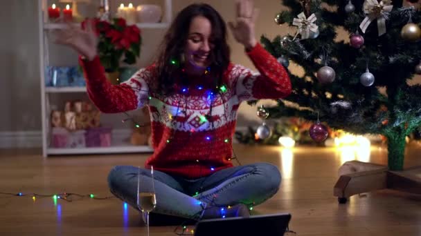 Amplio tiro alegre mujer caucásica feliz sentado en el árbol de Navidad decorado en la víspera de Año Nuevo en casa hablando en la tableta video chat tostadas beber champán. Jovencita alegre sonriendo celebrando. — Vídeo de stock