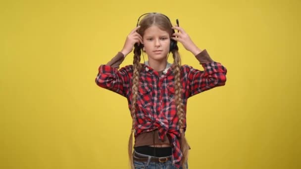Visão frontal grave adolescente concentrada colocando fones de ouvido com microfone olhando para a câmera. Retrato de adolescente adolescente caucasiano confiante posando em fundo amarelo. — Vídeo de Stock