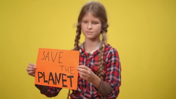 Save the planet banner in teenage Caucasian hands with blurred girl at yellow background turning looking around. Caring eco-activist posing with awareness message. Ecology protection concept. — Stockvideo