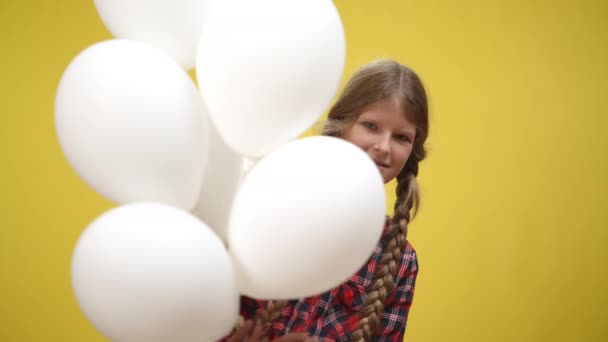 Hvite ballonger med sjarmerende, hvit tenåringsjente som kommer fram med gult smil. Vakker, slank tenåring i sakte film. Lykke- og gledebegrep. – stockvideo