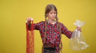 Sarı arka planda plastik torba ve çevre çantasıyla şüpheli bir genç kız. Sürdürülebilir yaşam tarzını seçen beyaz ergen portresi. Toplum ve ekoloji kavramı.
