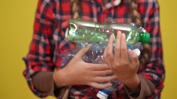 Tangan remaja tertutup dengan botol plastik bekas di latar belakang kuning. Remaja Kaukasia tak dikenal yang menyamar dengan sampah yang bisa didaur ulang. Konsep keberlanjutan dan ekologi. — Stok Video