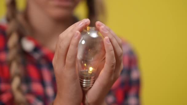 Lámpara de primer plano encendida en manos caucásicas adolescentes con fondo amarillo. Concepto de ideas e inteligencia. — Vídeos de Stock