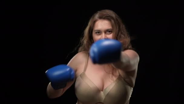Overgewicht vrouw in beha boksen schaduw kijken naar camera met ernstige gezichtsuitdrukking. Portret van een zwaarlijvige blanke volwassen dame die poseert op een zwarte achtergrond. Zelfverdediging en vechtsport. — Stockvideo