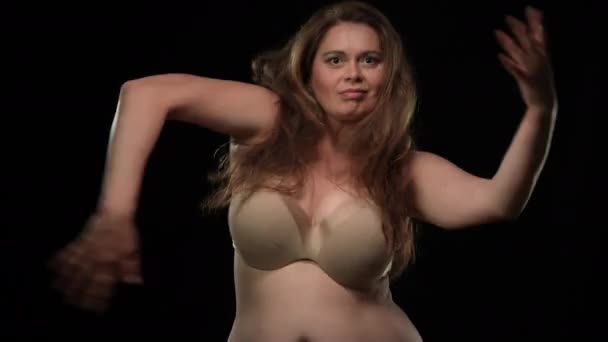 Joyful dans van vrolijke plus size vrouw op zwarte achtergrond. Portret van vrolijke zelfverzekerde glimlachende overgewicht blanke dame in ondergoed beha dansen op zoek naar camera. Diversiteit en lichaamspositief. — Stockvideo