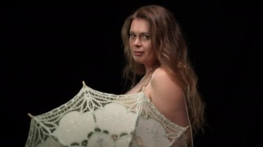 Erotik yüz ifadesiyle beyaz güneş şemsiyesini döndüren kameraya bakan kendinden emin ve iri yarı bir kadın. Siyah arka planda, aşırı kilolu, beyaz, baştan çıkarıcı kadının portresi. Tutku.