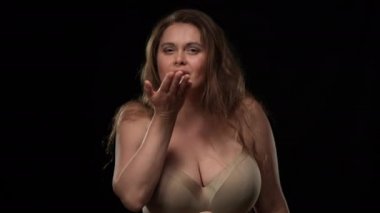 Baştan çıkarıcı artı boyunda bir kadın hava öpücüğü vererek siyah arka planda poz veriyor. Erotik yüz ifadesi olan kendine güvenen beyaz obez kadının portresi. Baştan çıkarma ve tutku kavramı