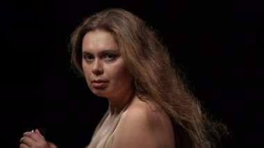 Yakın çekim, aşırı kilolu, saçları rüzgarla savrulan esmer kadın siyah arka planda poz veriyor. Sandalyeye oturmuş kameraya bakan iri yarı, baştan çıkarıcı beyaz kadın portresi..