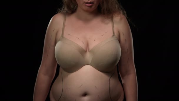 Nierozpoznawalna otyła kobieta rasy kaukaskiej ze śladami operacji plastycznych na ciele, patrząca na nożyczki w ręku. Nadwaga pani w bieliźnie przygotowuje się do zabiegu kosmetycznego na czarnym tle. — Wideo stockowe