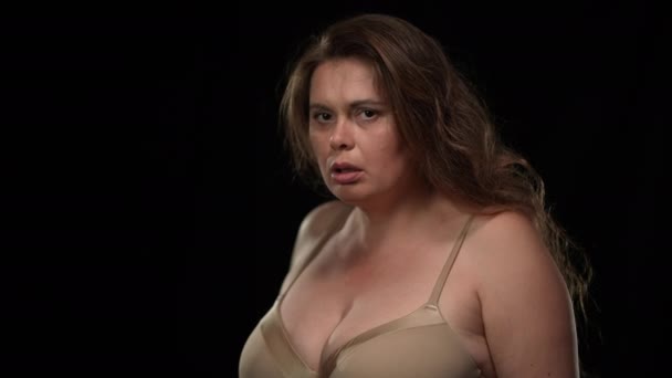 Side view scared overweight woman in underwear hiding from danger looking at camera with frightened facial expression closing with hands. Portrait of panicking Caucasian lady at black background. — Stockvideo