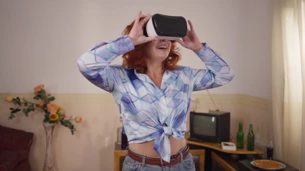 Excited Caucasian retro woman in vintage VR headset standing indoors admiring augmented reality. Portrait of happy carefree redhead lady enjoying leisure on weekend at home. — стоковое видео