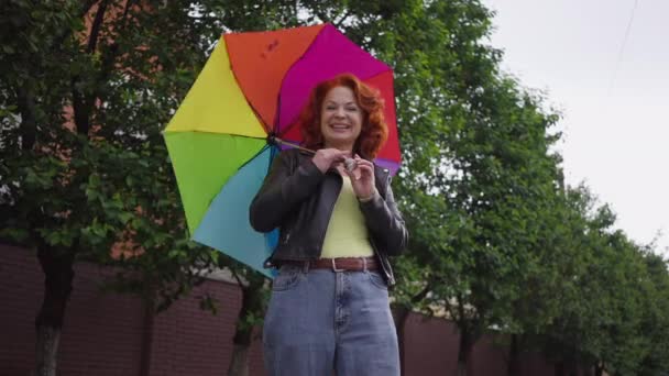 Happy confident beautiful retro woman spinning colorful umbrella standing on town street outdoors looking at camera smiling. Live camera zoom in in slow motion. — Stock video