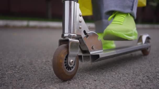 Close-up female foot in yellow green sneakers and denim jeans standing on retro kick scooter in slow motion. Unrecognizable confident skater outdoors on town street road. — Stockvideo