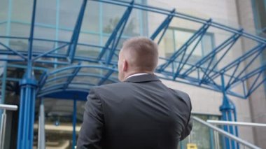 Back view confident young businessman talking on phone standing in front of business center. Successful Caucasian man discussing business in urban city outdoors. Intelligence and lifestyle.