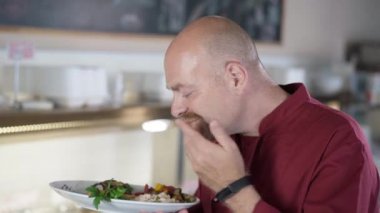 Tatmin olmuş erkek aşçı tabakta lezzetli bir yemek kokusu alıyor kameraya bakıp gülümsüyor. Kendi servis kafeteryasında kendine güvenen beyaz bir adamın portresi. Küçük işletme ve aşçılık kavramı.