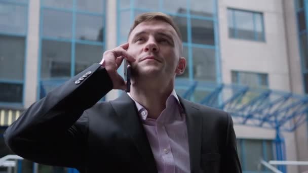Portrait d'un homme d'affaires confiant et positif parlant sur un smartphone debout à l'extérieur en ville. Beau succès élégant homme caucasien en costume noir avec téléphone au centre d'affaires. — Video