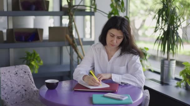 Fokuserad kvinna skriver med penna sitter vid bordet i café planering affärsstrategi. Porträtt av koncentrerad kaukasisk chef handstil idéer i slow motion tänkande. Långsamma rörelser. — Stockvideo