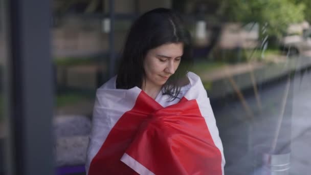 Gelukkige vrouw gewikkeld in Canadese vlag kijkend naar een camera die glimlacht terwijl ze binnen staat. Schieten door het raam van trotse, zelfverzekerde jongedame die poseert met de nationale vlag in slow motion. Patriottisme. — Stockvideo