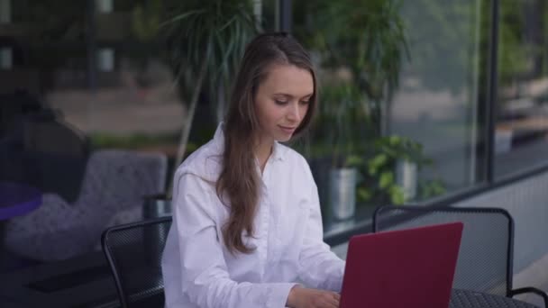 Młoda pozytywna kobieta siedząca przy stole z laptopem witająca przyjaciela spotykającego się w kawiarni na świeżym powietrzu. Kaukascy przyjaciele na przerwie obiadowej w miejskim mieście na letnim tarasie w kawiarni. Zwolniony ruch. — Wideo stockowe