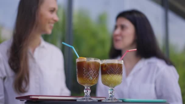 Vitamin cocktails on table in sidewalk cafe with two blurred female friends chatting at background. Young Caucasian women meeting for lunch in urban city talking smiling. Leisure concept. — Stock Video