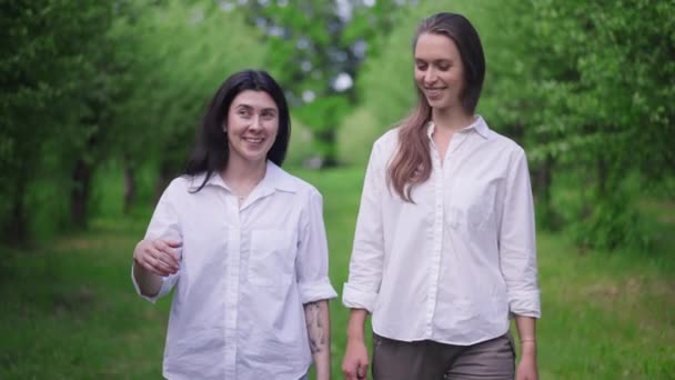 フロントビュードリー2人の若い女性のスローモーション屋外で歩いて撮影した。春の夏の公園散策でおしゃべりするのんびりした白人の友人の肖像画休憩を楽しむ. — ストック動画