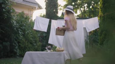 Geniş açılı kendine güvenen beyaz kadın arka bahçedeki masaya sebze sepetiyle yürüyor. Bahçede kirli çamaşırları dışarıda asılı, zayıf, çekici bir bayan. Kırsal yaşam tarzı kavramı.