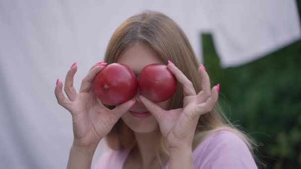 Vidám fiatal nő szórakozás pózol piros paradicsom a szabadban mosolyogva. Portré vidám karcsú gyönyörű kaukázusi Y-generációs hölgy borító szemét zöldség nézi kamera. — Stock videók