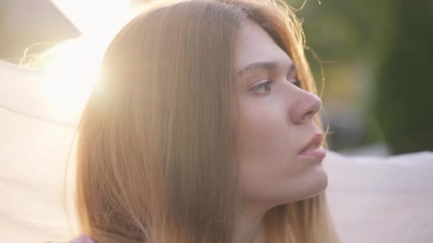 Cabeza joven hermosa mujer caucásica posando en rayos de sol con bufanda blanca en cámara lenta. Cámara en vivo alejarse de la hermosa dama confiada disfrutando de la puesta del sol en el patio trasero al aire libre. — Vídeo de stock