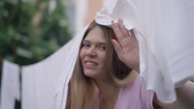 Beyaz, temiz çamaşırları dışarıda ipe asılmış neşeli, beyaz bir kadın kameraya bakıp gülümsüyor. Bahçede eğlenen neşeli, mutlu, zayıf, çekici kadının portresi..