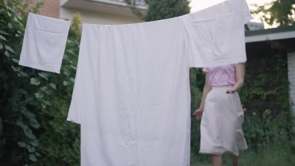 ロープと離れる上できれいな新鮮な洗濯乾燥を渡す裏庭で実行している楽しいスリムな若い女性。明るい白人女性が春の夏の日を屋外で楽しむ. — ストック動画