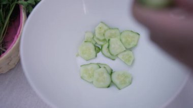 Ağır çekimde salatalık doğrayan kadın elli beyaz kâse. Sağlıklı vejetaryen salatası pişiren tanınmayacak kadar zayıf genç bir kadın. Vejetaryenlik ve yaşam tarzı konsepti.
