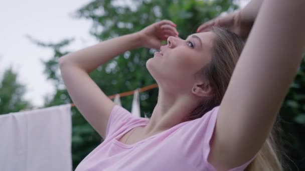 Självsäker kvinna kastar hår i slow motion tittar på kameran står på bakgården med ren fräsch tvätt torkning i bakgrunden. Porträtt av vacker smal vit hemmafru poserar utomhus. — Stockvideo