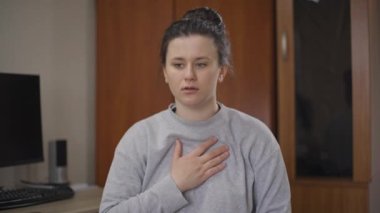 Nefes darlığı çeken, göğsüne dokunan, şok olmuş yüz ifadesini soluyan beyaz bir kadın. İçeride poz veren çekici bir kadının portresi. Panik atak ve stres konsepti.