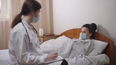 Yatakta yatan genç hasta kadın hastane koğuşundaki bulanık profesyonel doktorun sorularını yanıtlıyor. Sağlık geçmişi yazan yorgun, kafkasyalı bir hastanın portresi..