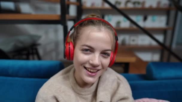 Großaufnahme fröhliches Teenager-Mädchen, das Musik mit Kopfhörern genießt und lächelnd in die Kamera schaut. Porträt eines fröhlichen hübschen kaukasischen Teenagers, der zu Hause Spaß hat. Lifestyle- und Freizeitkonzept. — Stockvideo