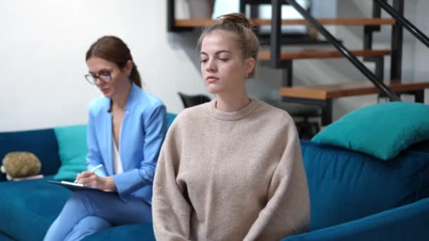 Chica adolescente de tiro medio mirando hacia atrás al terapeuta borroso girando mirando a la cámara sonriendo. Retrato de adolescente caucásico feliz posando en el interior de la oficina de psicólogos. Alivio y concepto de terapia. — Vídeo de stock