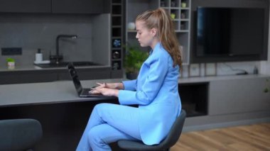 Yan görünüş, resmi takım elbiseli serbest çalışanın evde mutfaktaki dizüstü bilgisayarda daktilo kullanmasına yoğunlaşmıştı. Çevrimiçi internet sörfü yapan, kendinden emin, beyaz, genç bir kadın..