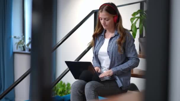 Charmant schattig tienermeisje luisteren naar muziek in hoofdtelefoon berichten online in sociale media op laptop. Side view portret van ontspannen Kaukasische tiener genieten van recreatieve surfen Internet thuis — Stockvideo