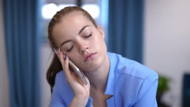 Joven mujer de negocios aburrida bostezando hablando por teléfono en el interior. Retrato de vista frontal de mujer hermosa caucásica desinteresada en elegante traje azul. Inquietud y aburrimiento. — Vídeo de stock
