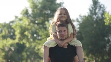 Ön manzara tatmin olmuş genç bir adamın omuzlarında konuşan kız dışarıda güneşin altında gülümsüyor. Güzel beyaz kız bahar parkında babasıyla eğleniyor..