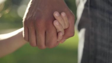 Erkek eli, gün ışığında küçük dişi avucunu tutuyor. Güneşli bahar parkında duran tanınmayan beyaz baba ve kızı. Aile birliği ve birliktelik kavramı.