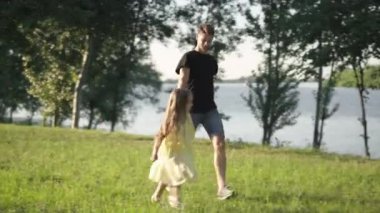 Sunny Park 'ta koşan neşeli kız genç adamın elini tutuyor. Neşeli, beyaz bir kızın hafta sonları dışarıda babasıyla eğlenirken görüntüsü. Çocukluk ve aile.